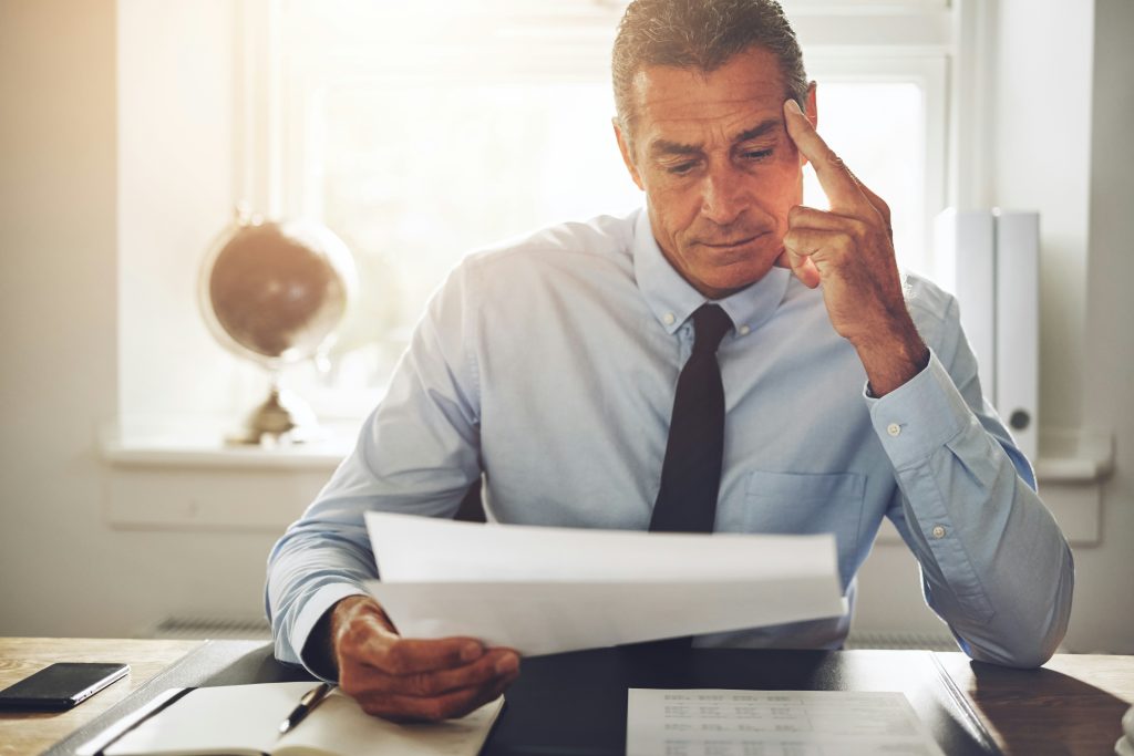 A man in a shirt and tie sits at a desk, reviewing papers in a professional office setting.