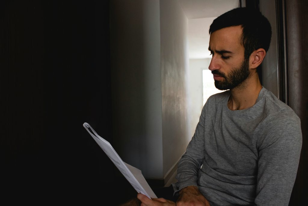 A man sits on a chair, engrossed in reading a document.